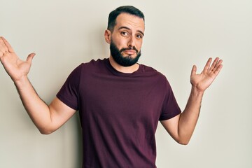 Fototapeta premium Young man with beard wearing casual t shirt clueless and confused with open arms, no idea and doubtful face.