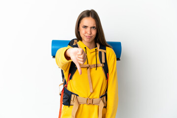 Young mountaineer woman with a big backpack over isolated white background showing thumb down with...