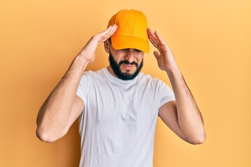 Young man with beard wearing yellow cap with hand on head, headache because stress. suffering migraine.