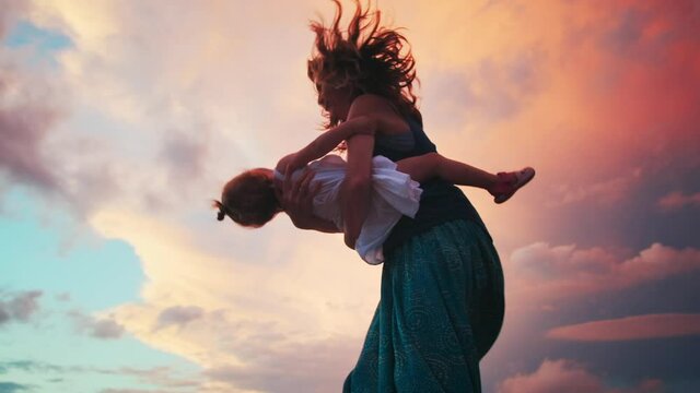Family dances on pier. Woman and toddler girl dance and spin on the wooden pier during sunset