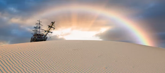 Poster Silhouet van oud schip op woestijn met regenboog bij verbazende zonsondergang © muratart