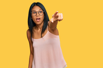 Young african american woman wearing casual clothes and glasses pointing with finger surprised ahead, open mouth amazed expression, something on the front