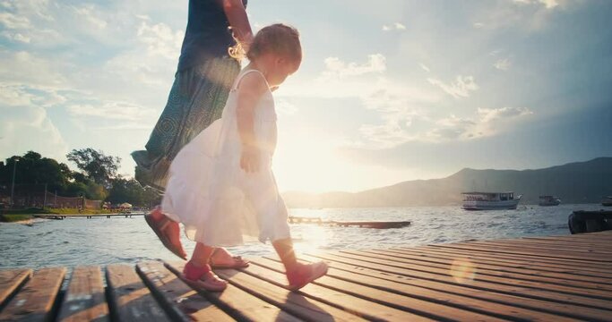 Family walk on pier. Woman and toddler girl walk on the wooden pier at sunset