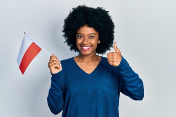 Young african american woman holding poland flag smiling happy and positive, thumb up doing excellent and approval sign