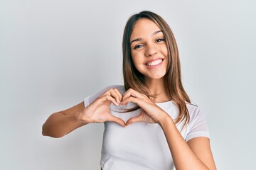 Young brunette woman wearing casual white t shirt smiling in love doing heart symbol shape with hands. romantic concept.
