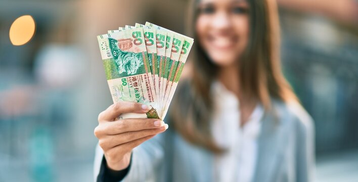Young latin businesswoman smiling happy holding hong kong dollars at the city.