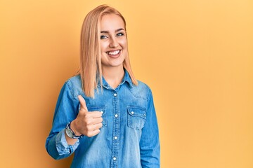 Beautiful caucasian woman wearing casual denim jacket doing happy thumbs up gesture with hand. approving expression looking at the camera showing success.