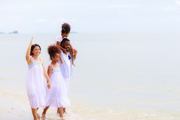 Fototapeta na wymiar Happy African american family holding hands and walking together on the beach during holiday.