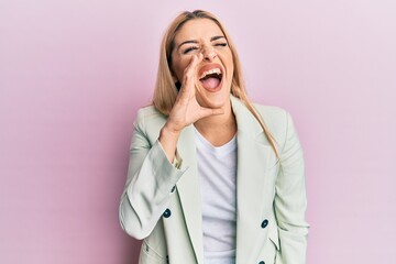 Young caucasian woman wearing business clothes shouting and screaming loud to side with hand on mouth. communication concept.
