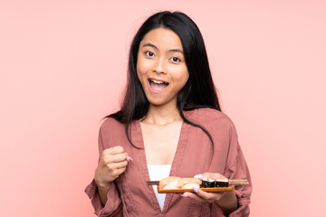 Teenager Asian girl eating sushi isolated on pink background celebrating a victory