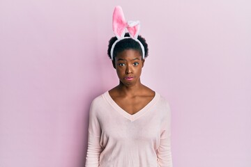 Young african american girl wearing cute easter bunny ears puffing cheeks with funny face. mouth inflated with air, crazy expression.