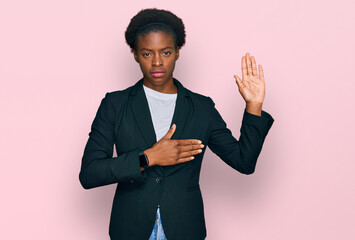 Young african american girl wearing business clothes swearing with hand on chest and open palm,...