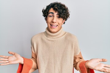 Hispanic young man wearing casual winter sweater clueless and confused expression with arms and...