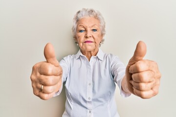 Senior grey-haired woman doing thumbs up positive gesture relaxed with serious expression on face. simple and natural looking at the camera.