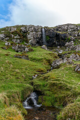 Fototapeta na wymiar Creek waterfall under the clouds, Faroe Islands.