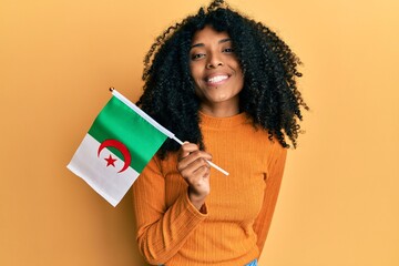 African american woman with afro hair holding algeria flag looking positive and happy standing and smiling with a confident smile showing teeth