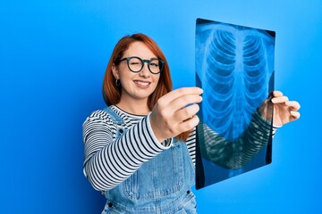 Beautiful redhead woman holding chest radiography winking looking at the camera with sexy...