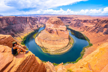 A French tourist sitting on Horseshoe Bend and the Colorado River in the background, Arizona. United States.