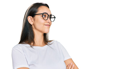 Young hispanic woman wearing casual white t shirt looking to the side with arms crossed convinced and confident