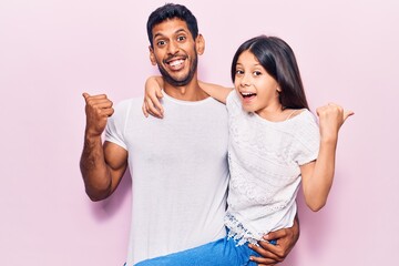 Latin father and daughter wearing casual clothes pointing thumb up to the side smiling happy with open mouth - obrazy, fototapety, plakaty