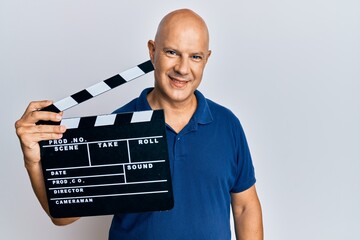 Middle age bald man holding video film clapboard looking positive and happy standing and smiling...