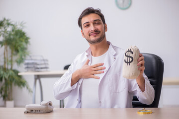 Young male doctor holding moneybag in remuneration concept