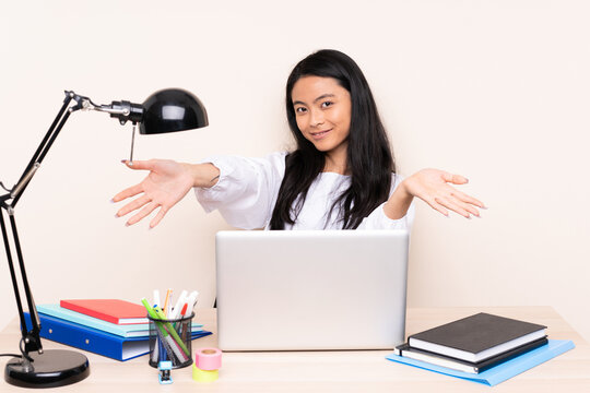 Student asian girl in a workplace with a laptop isolated on beige background presenting and inviting to come with hand