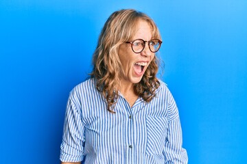 Plakat Middle age blonde woman wearing casual clothes and glasses angry and mad screaming frustrated and furious, shouting with anger. rage and aggressive concept.