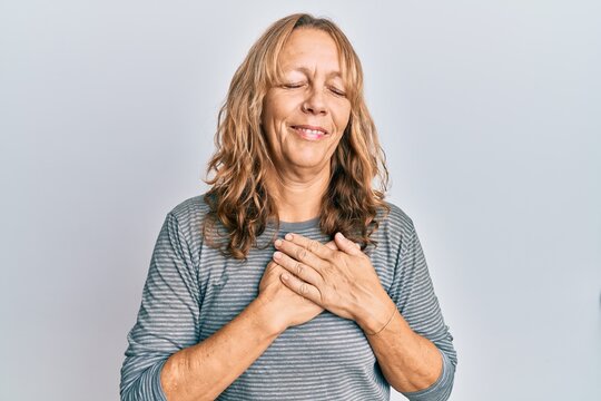 Middle age blonde woman wearing casual clothes smiling with hands on chest, eyes closed with grateful gesture on face. health concept.