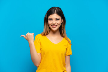 Young Russian girl isolated on blue background pointing to the side to present a product
