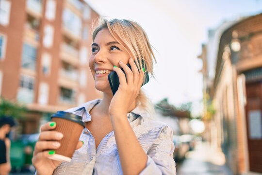 Young blonde woman smiling happy talking on the smartphone and drinking take away coffee at the city.