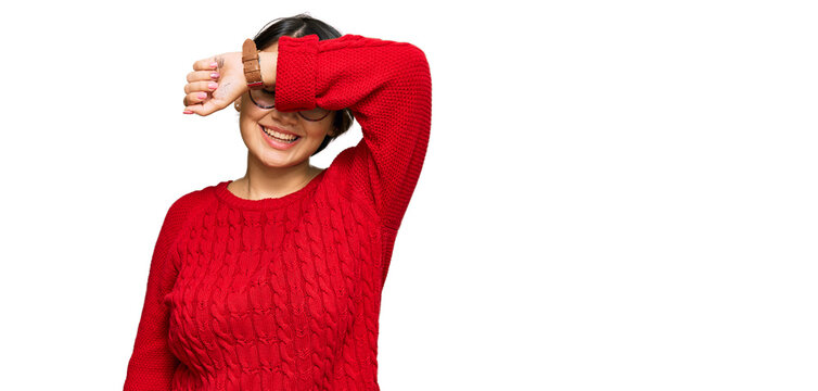 Young beautiful hispanic woman with short hair wearing casual sweater and glasses covering eyes with arm smiling cheerful and funny. blind concept.
