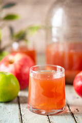 Glass of fresh apple juice and red apples on wooden background