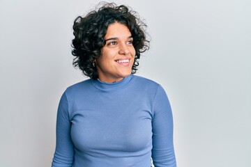 Fototapeta na wymiar Young hispanic woman with curly hair wearing casual clothes looking to side, relax profile pose with natural face and confident smile.