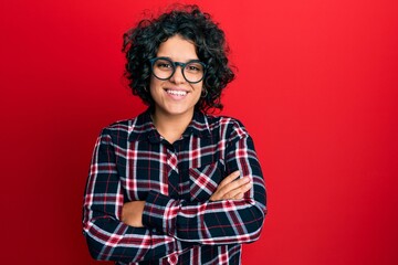 Young hispanic woman with curly hair wearing casual clothes and glasses happy face smiling with crossed arms looking at the camera. positive person.