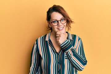 Young caucasian woman wearing casual clothes and glasses looking confident at the camera smiling with crossed arms and hand raised on chin. thinking positive.