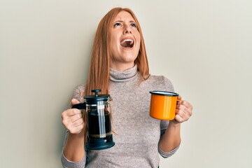 Young irish woman drinking italian coffee angry and mad screaming frustrated and furious, shouting with anger looking up.