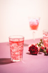 Red drink cocktail or lemonade with ice in a glass on pink background.