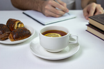 A cup of tea with lemon on a light background. Snack at work. A cup of tea at work. Cup of tea with pastries