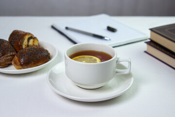 A cup of tea with lemon on a light background. Snack at work. A cup of tea at work. Cup of tea with pastries