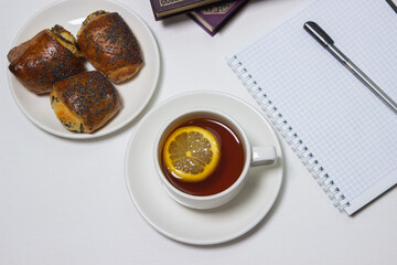 A cup of tea with lemon on a light background. Snack at work. A cup of tea at work. Cup of tea with pastries