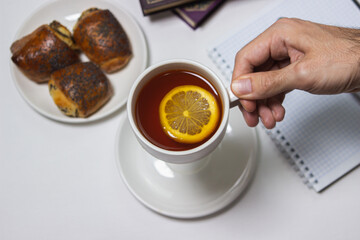 A cup of tea with lemon on a light background. Hand holds a cup of tea. Snack at work. A cup of tea at work.
