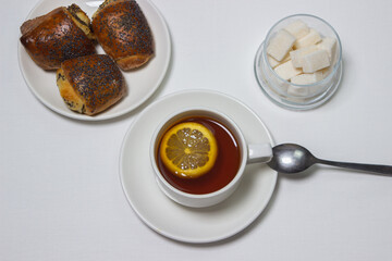 A cup of tea with lemon on a light background. Snack at work. A cup of tea at work. Cup of tea with pastries
