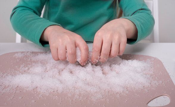 Laboratory, chemical experiments day 2 of 14. Children's hands squeeze white artificial snow from sodium polyacrylate scattered on the table, close-up