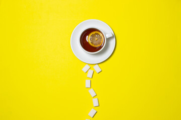 A cup of tea with lemon on a yellow background. Creative photography of tea with sugar. Sugar cubes next to tea