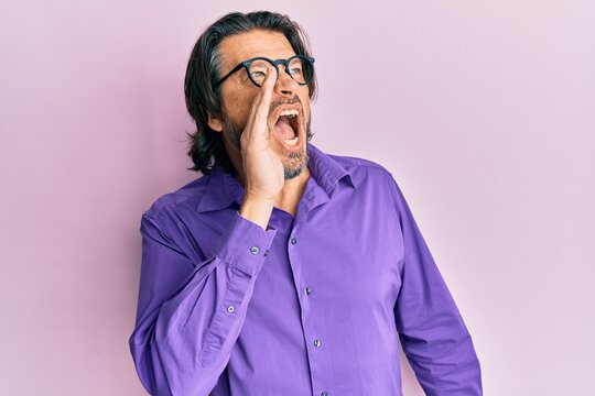 Middle age handsome man wearing casual clothes and glasses shouting and screaming loud to side with hand on mouth. communication concept.