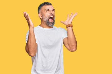 Fototapeta premium Middle age handsome man wearing casual white tshirt celebrating mad and crazy for success with arms raised and closed eyes screaming excited. winner concept