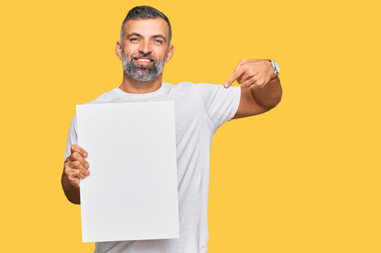 Middle age handsome man holding blank empty banner pointing finger to one self smiling happy and proud
