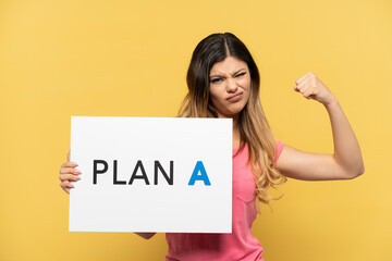 Young Russian girl isolated on yellow background holding a placard with the message PLAN A doing strong gesture