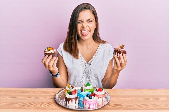 Young caucasian woman holding cake slices sticking tongue out happy with funny expression.